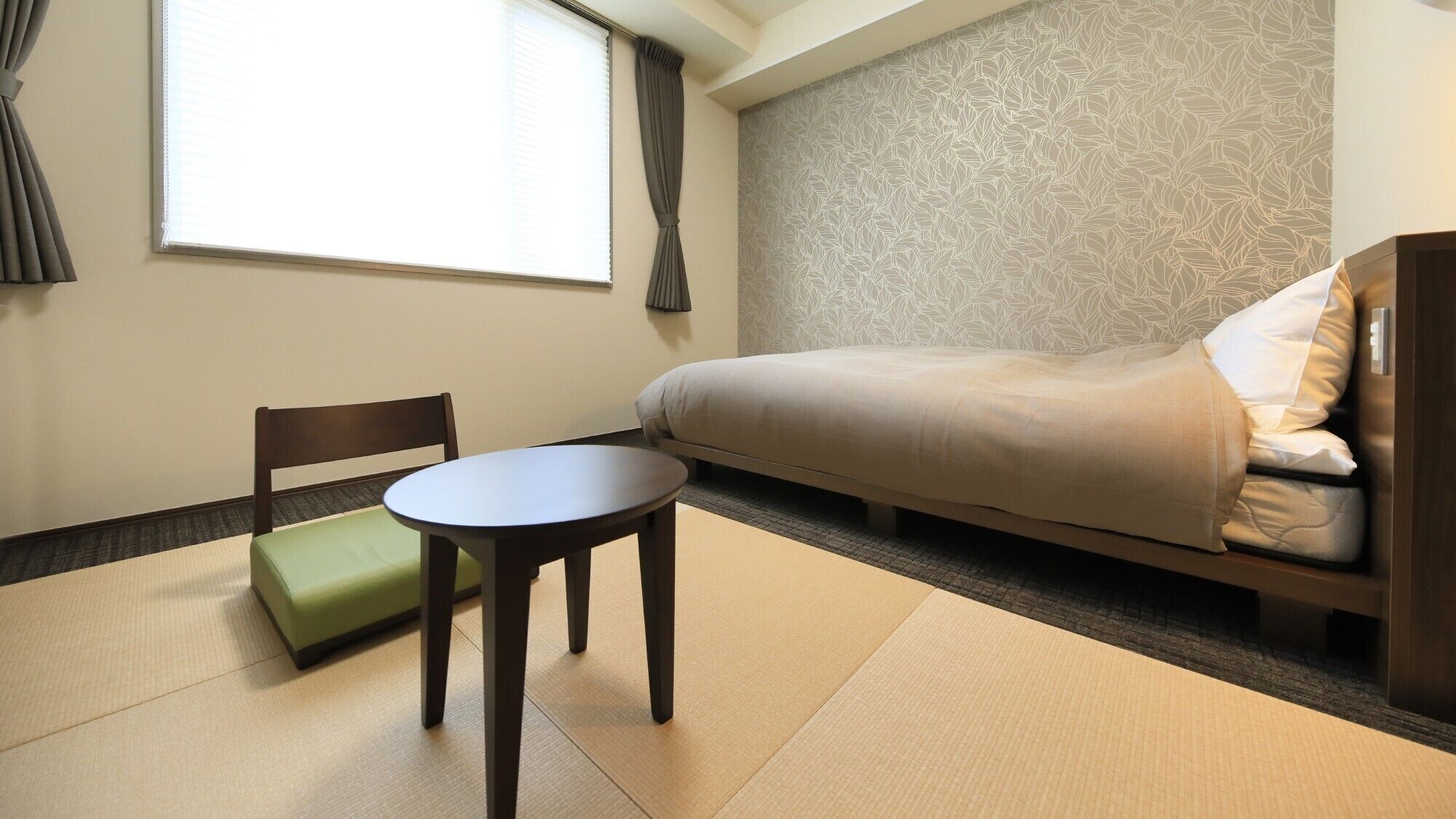 Une chambre d’hôtel avec un lit, une chaise, une petite table et une fenêtre avec des rideaux.