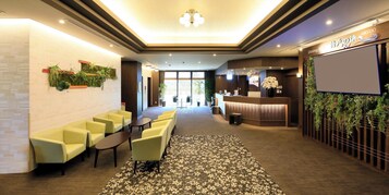 Um saguão de hotel com balcão de recepção, área de estar e plantas decorativas.