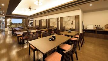 A spacious dining area with multiple tables and chairs, a ceiling fan, and a view of the outdoors.