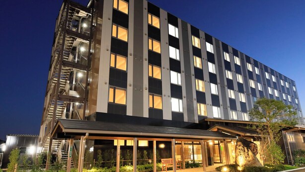Un hôtel moderne à l’architecture imposante, avec plusieurs étages, un hall d’entrée abrité et une façade bien éclairée.
