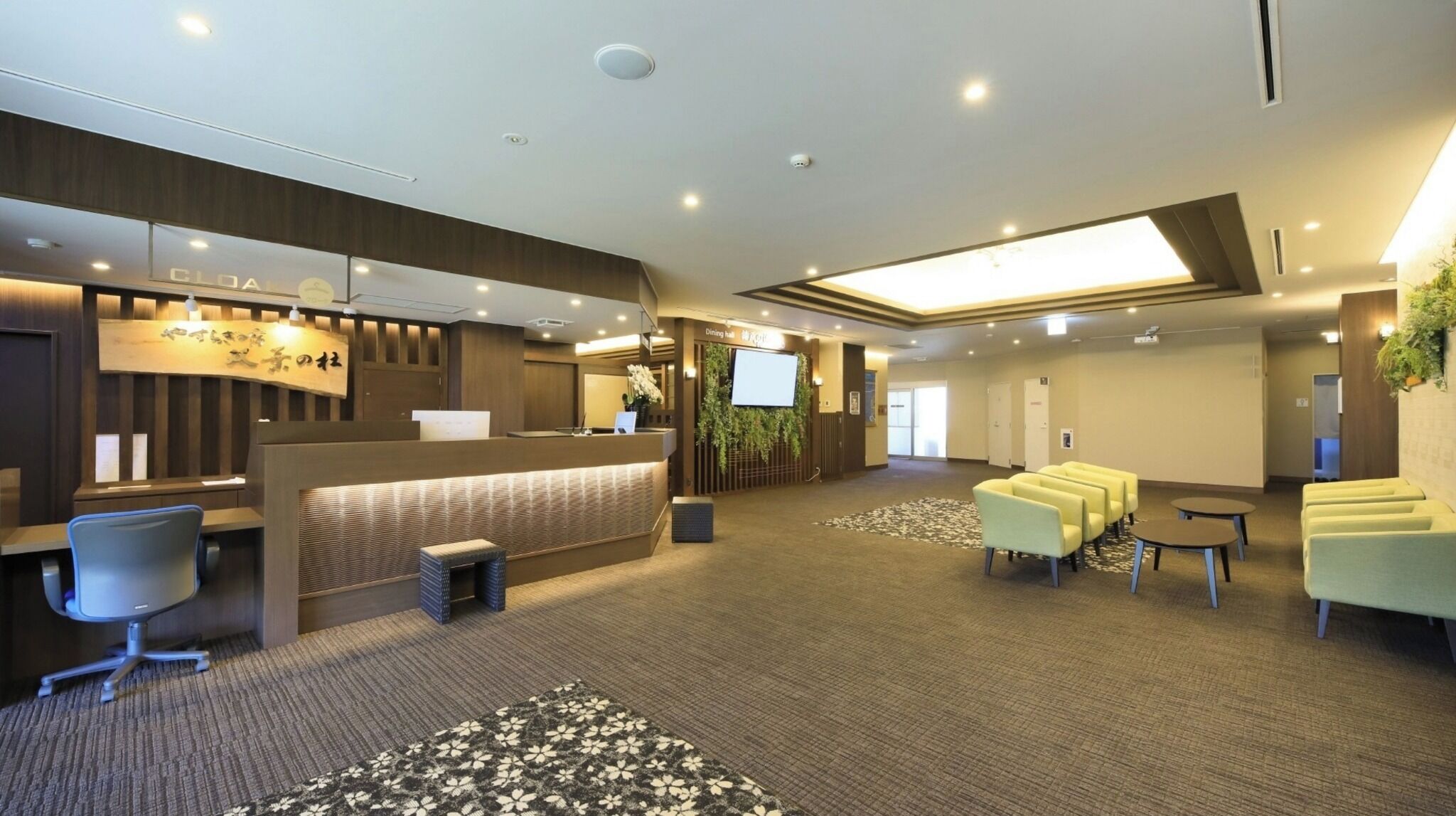 Un hall d’hôtel comprenant un comptoir d’accueil, un espace salon et un grand écran.