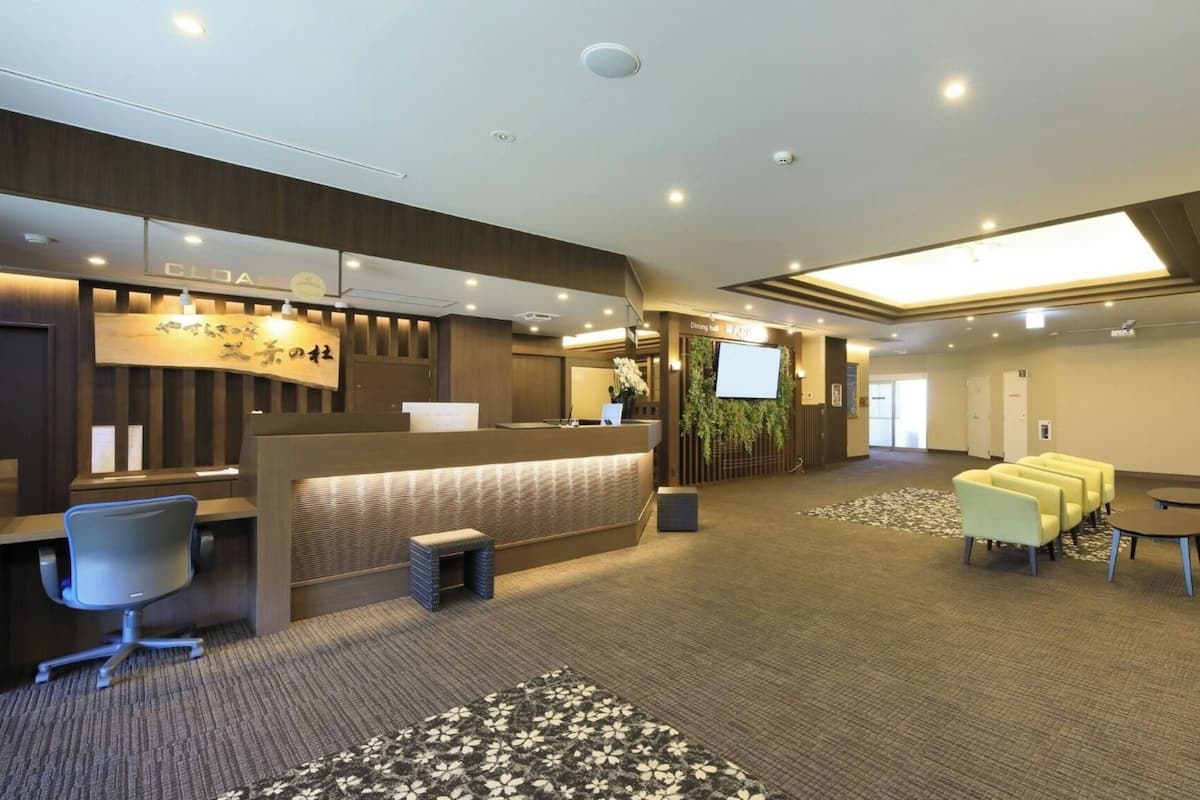 Eine Hotelhalle mit Rezeption, Sitzgelegenheiten und einem großen Bildschirm.