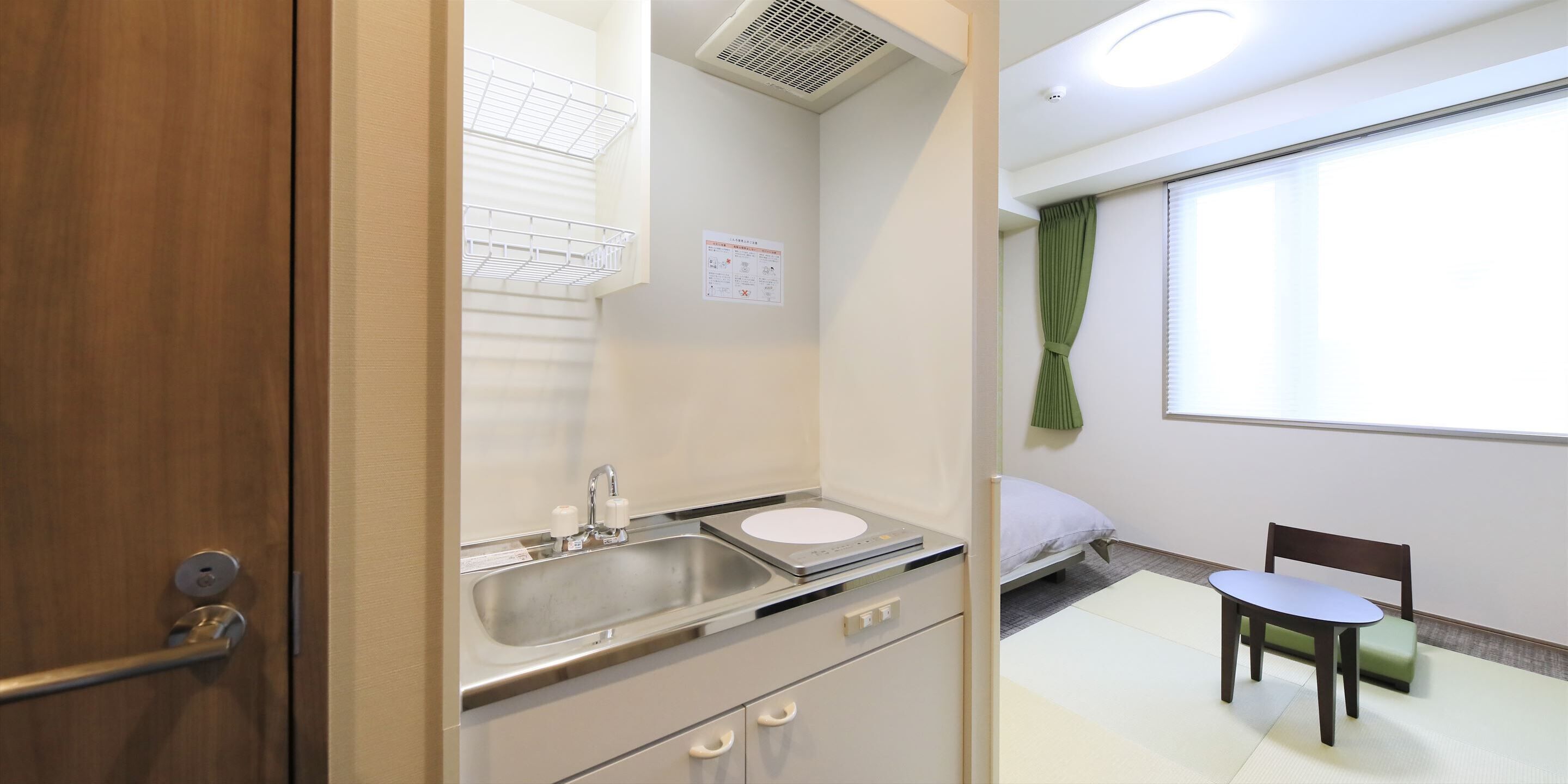A compact hotel room with a kitchenette, a single bed, a small table, and a chair.