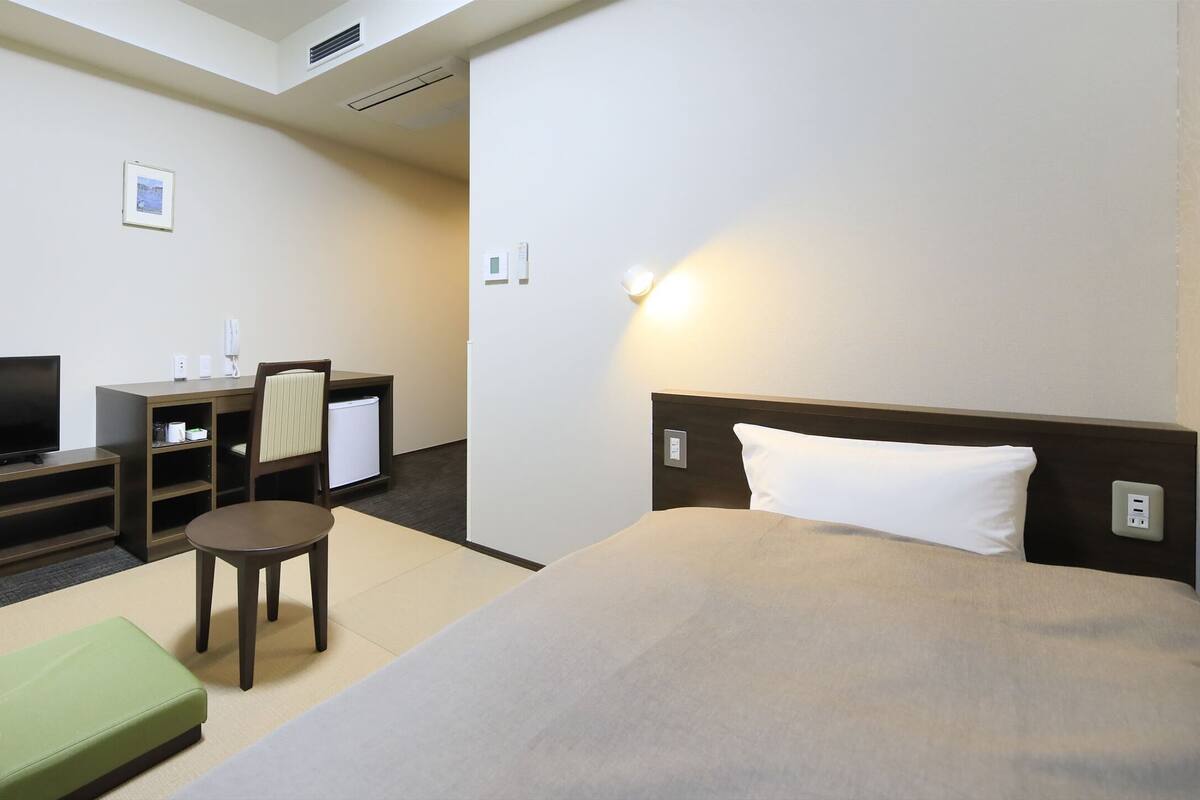 Ein Hotelzimmer mit einem Bett, einem Fernseher, einem Schreibtisch, einem Sessel und einem kleinen Tisch.