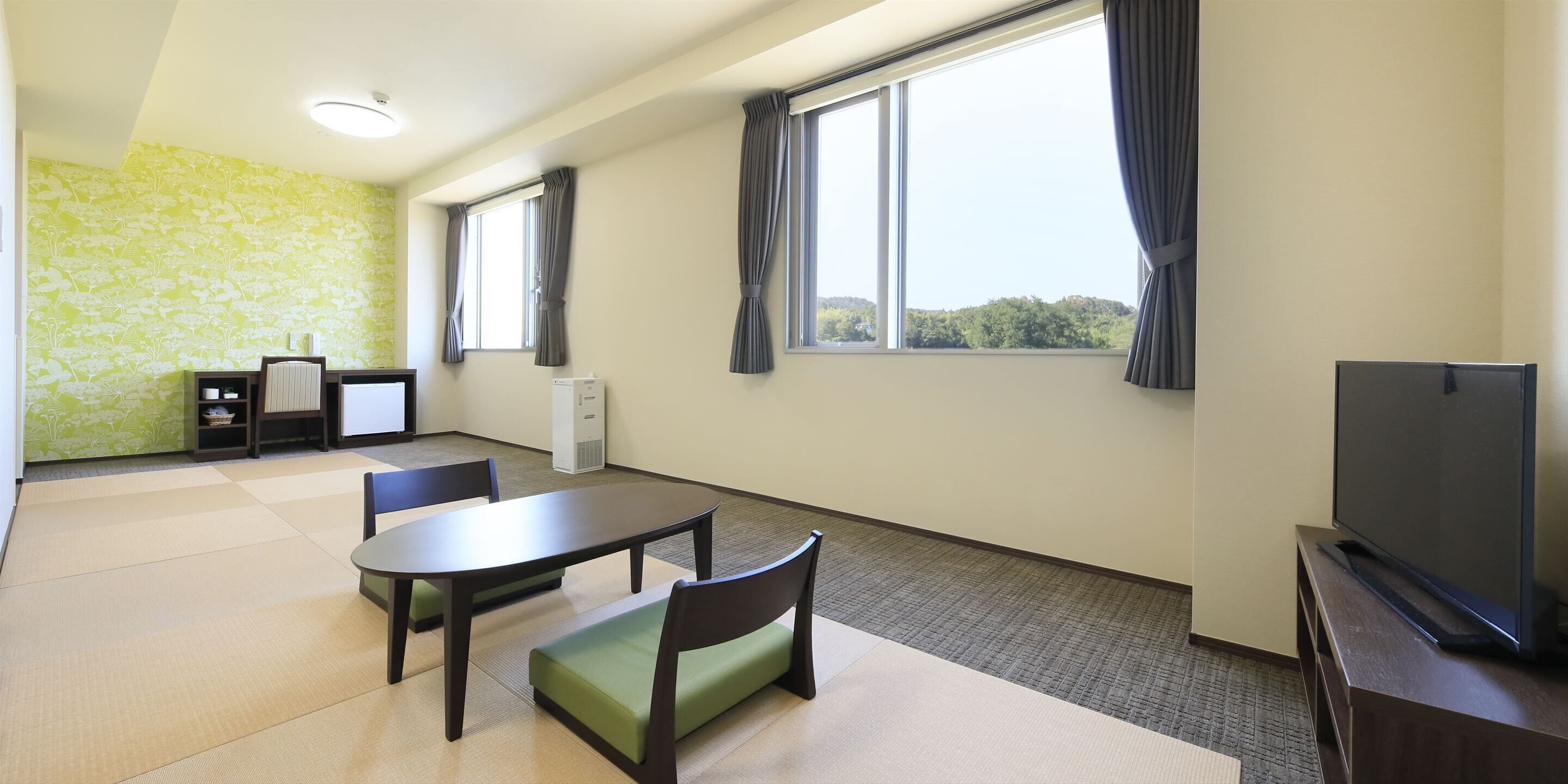Una habitación con un ventanal grande, un televisor de pantalla plana, una mesa con sillas y un mueble pequeño.