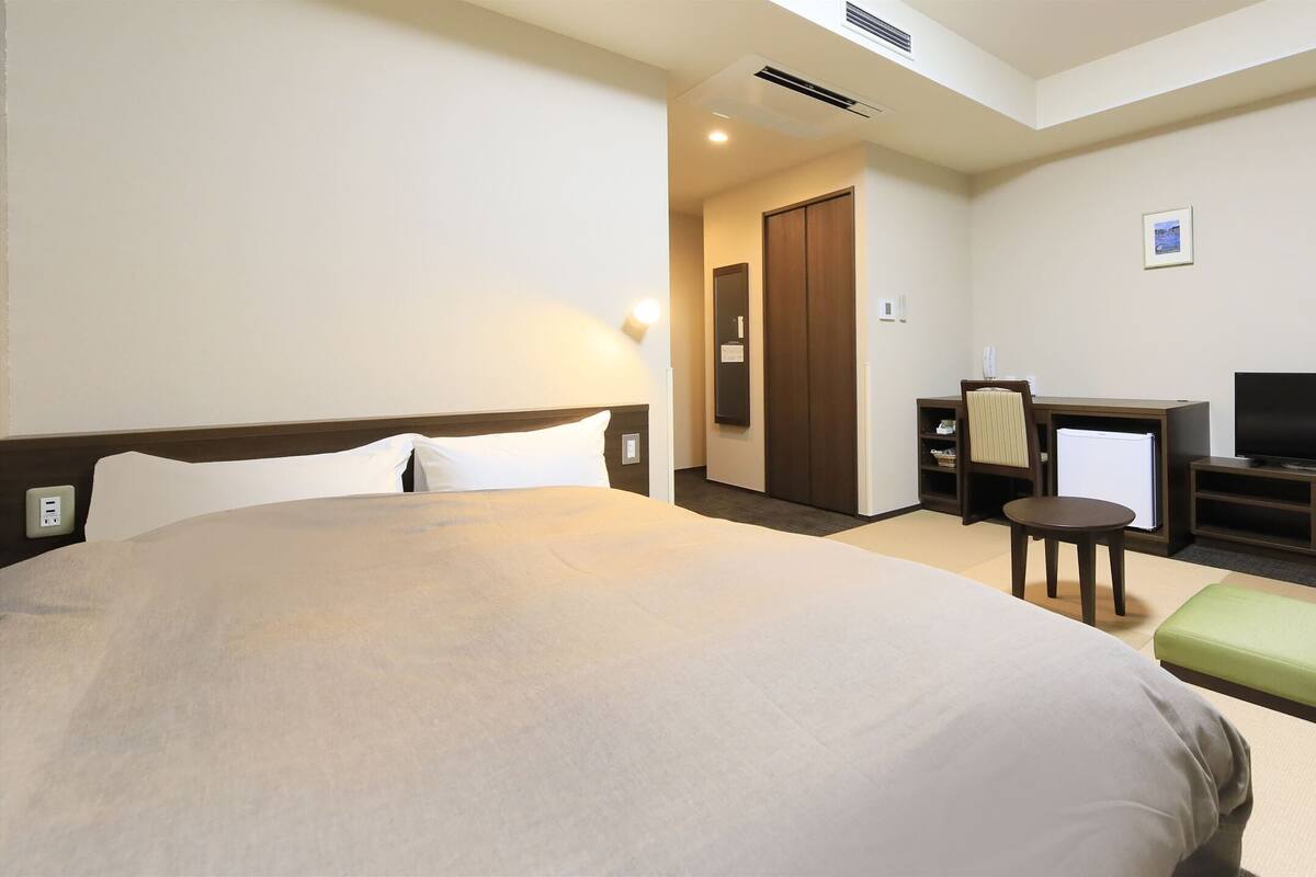 Ein Hotelzimmer mit einem großen Bett, einem Schreibtisch mit Stuhl, einem Fernseher und einem kleinen Kühlschrank.