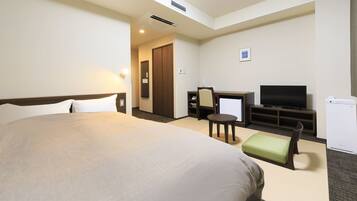 Habitación de hotel con una cama grande, un escritorio con silla, televisor y un refrigerador pequeño.