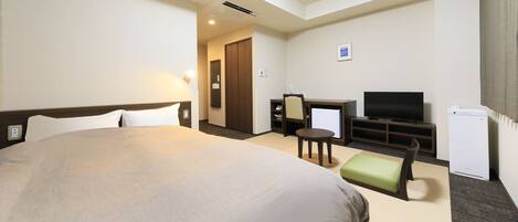 A hotel room with a large bed, a desk with a chair, a television, and a small refrigerator.