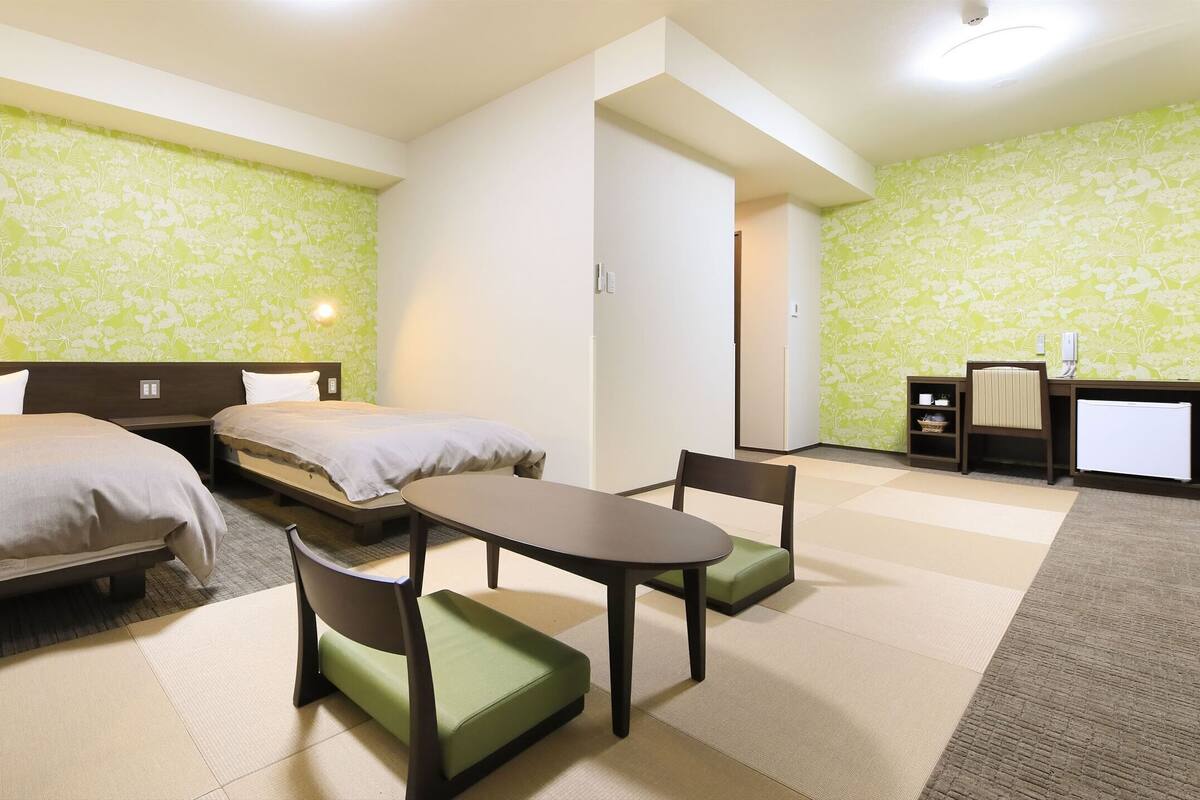 Ein Hotelzimmer mit zwei Betten, einem kleinen Tisch, Stühlen und einem Schreibtisch mit Sitzgelegenheit.