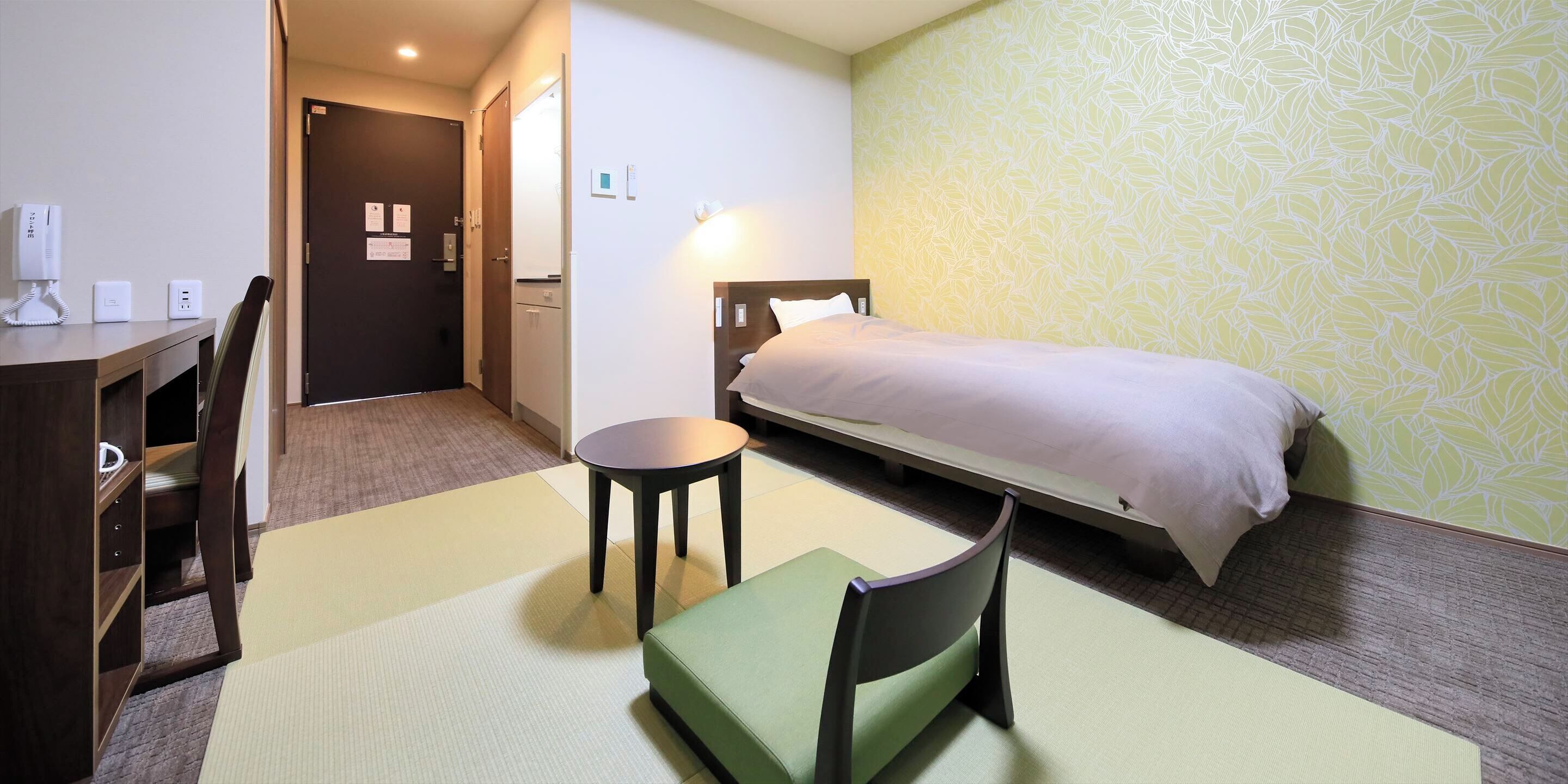 A hotel room with a bed, a desk, a chair, and a small table.