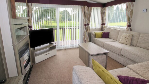 A living room with a flat-screen TV, a sofa set, a coffee table, and a TV stand. - Swan (Leominster)
