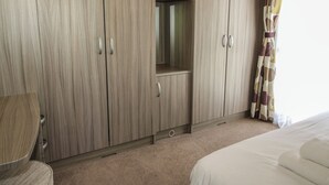 A bedroom with a large bed, a wardrobe, a chair, and a window with curtains. - Swan (Leominster)
