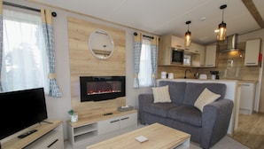 A modern living room with a flat-screen TV, a fireplace, a grey sofa, and a wooden coffee table.