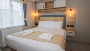 A neatly made bed with white linens and a beige throw, a wooden headboard, and two bedside tables with lamps.
