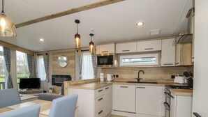 A modern kitchen with white cabinets, a wooden countertop, and a built-in stove. There is a dining area with a table and chairs, and a TV mounted on the wall.