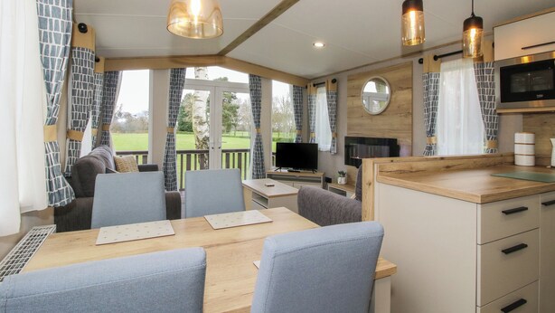 A modern kitchen with a dining area, large windows, and a TV.
