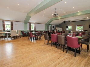A spacious dining area with multiple tables and chairs, a high ceiling with recessed lighting, and large windows allowing natural light. - Owl (Leominster)