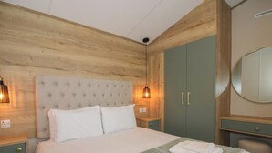A neatly made bed with white linens and two folded towels, a wooden headboard, a green patterned bedspread, and a green wardrobe with two doors. - Owl (Leominster)