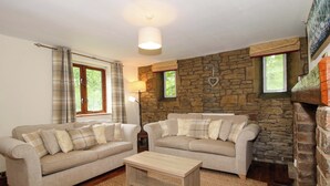 A living room with two sofas, a coffee table, a stone wall, and a fireplace. - Stables Cottage (Leominster)