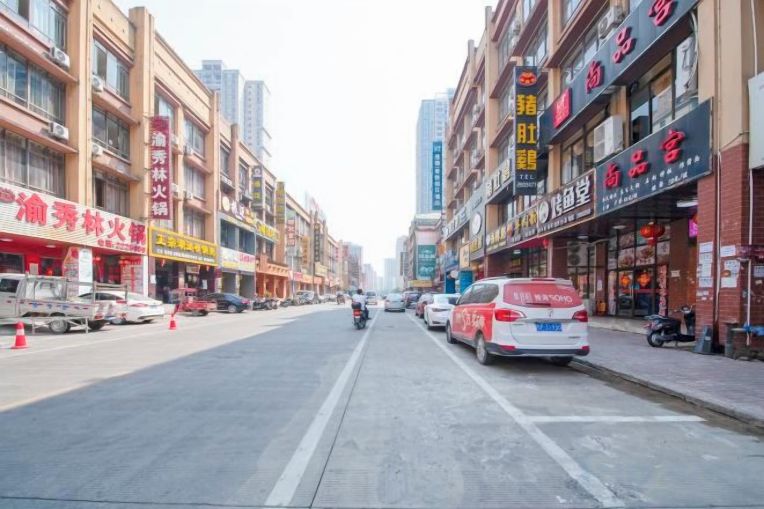 A street with shops on both sides, a motorbike in the center, and a white car parked on the right.