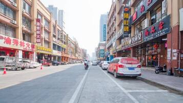 A street with shops on both sides, a motorbike in the center, and a white car parked on the right.