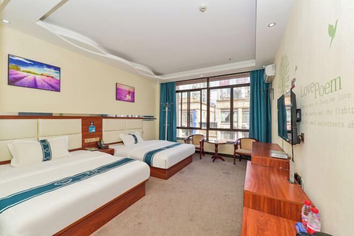 Habitación de hotel con dos camas, un escritorio, una silla y ventanas grandes.