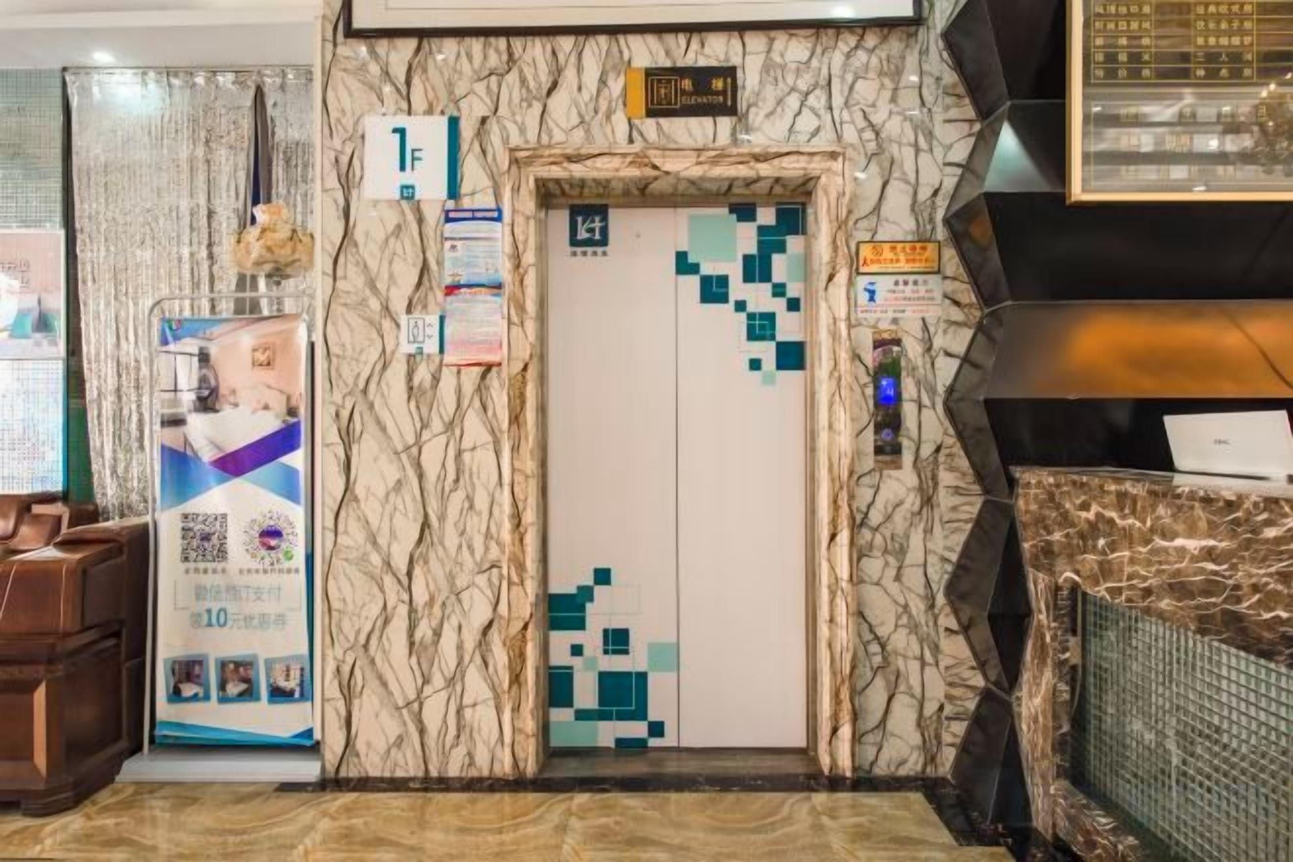 A hotel lobby with a marble wall, an elevator, a reception desk, and a QR code stand.