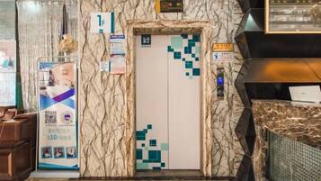 A hotel lobby with a marble wall, an elevator, a reception desk, and a QR code stand.