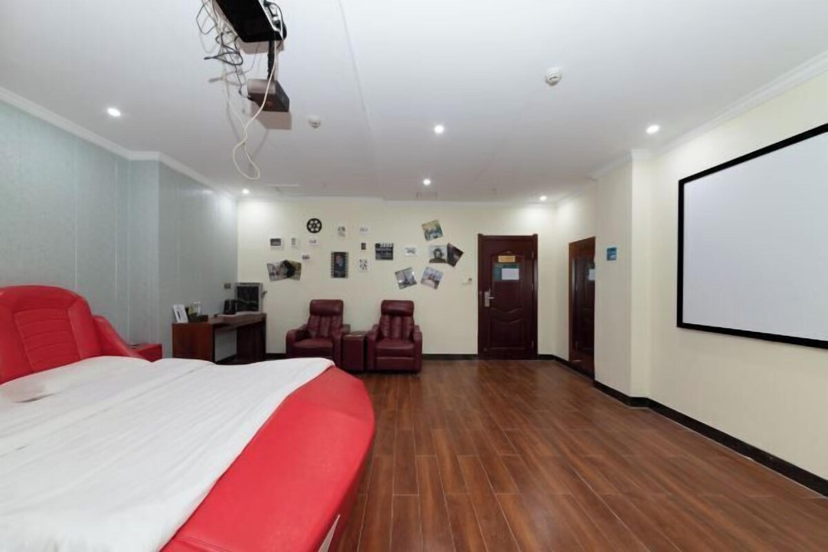 Habitación de hotel con una cama, un escritorio, dos sillas, un proyector y una pantalla en la pared.