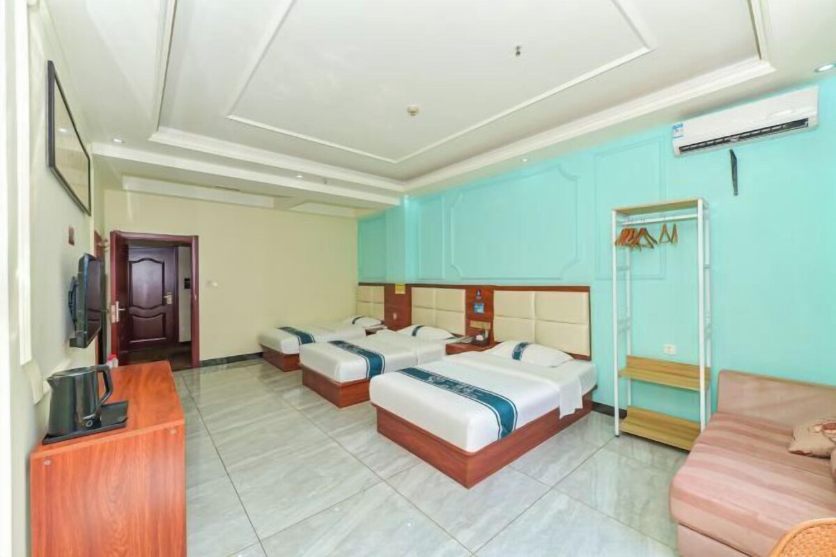 Habitación de hotel con tres camas, un escritorio de madera, televisor y aire acondicionado.