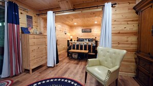Interior de una cabaña de madera con un sillón de cuero, una mesa de comedor de madera y una bandera en la pared.