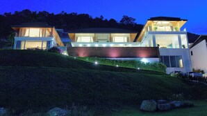 Una moderna casa a due piani con ampie finestre e tetto piatto, circondata da un giardino curato e dolci colline.