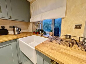 A kitchen with a wooden countertop, a white sink, and a window with a view of greenery outside. - Style House Luxury Cottage (Jameston)
