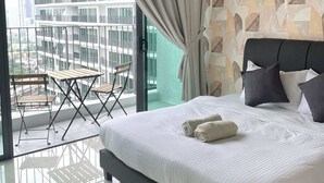 Un dormitorio moderno con una cama grande, un balcón con mesa y sillas, y vistas a un edificio de gran altura.