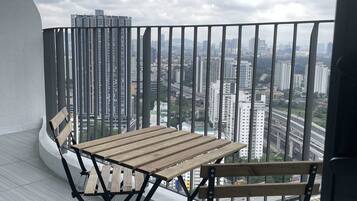 A balcony with a wooden table and chairs, overlooking a cityscape with high-rise buildings.