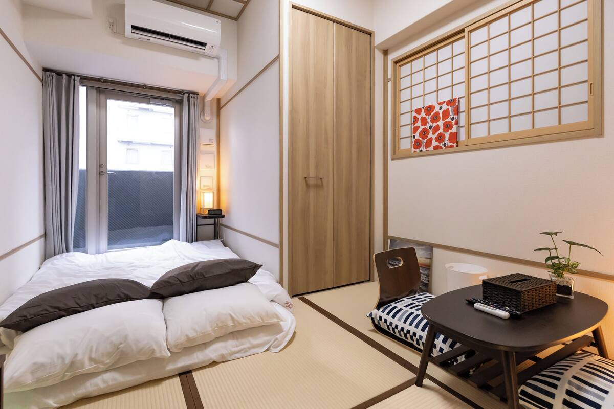 Une chambre d’hôtel avec un lit, une petite table sur laquelle se trouve une télécommande, une plante et une porte coulissante.
