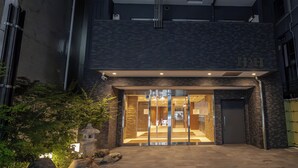 A modern building entrance with a glass door, a brick facade, and a small pagoda-like structure in the garden. - H2H SHINSAIBASHI I (Osaka)