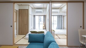 A modern hotel room with a sofa, a small table, and a chair. There are two beds with curtains and a window. - H2H SHINSAIBASHI I (Osaka)
