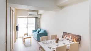 A modern dining area with a table set for four, a blue sofa, and a cityscape painting on the wall. - H2H SHINSAIBASHI I (Osaka)
