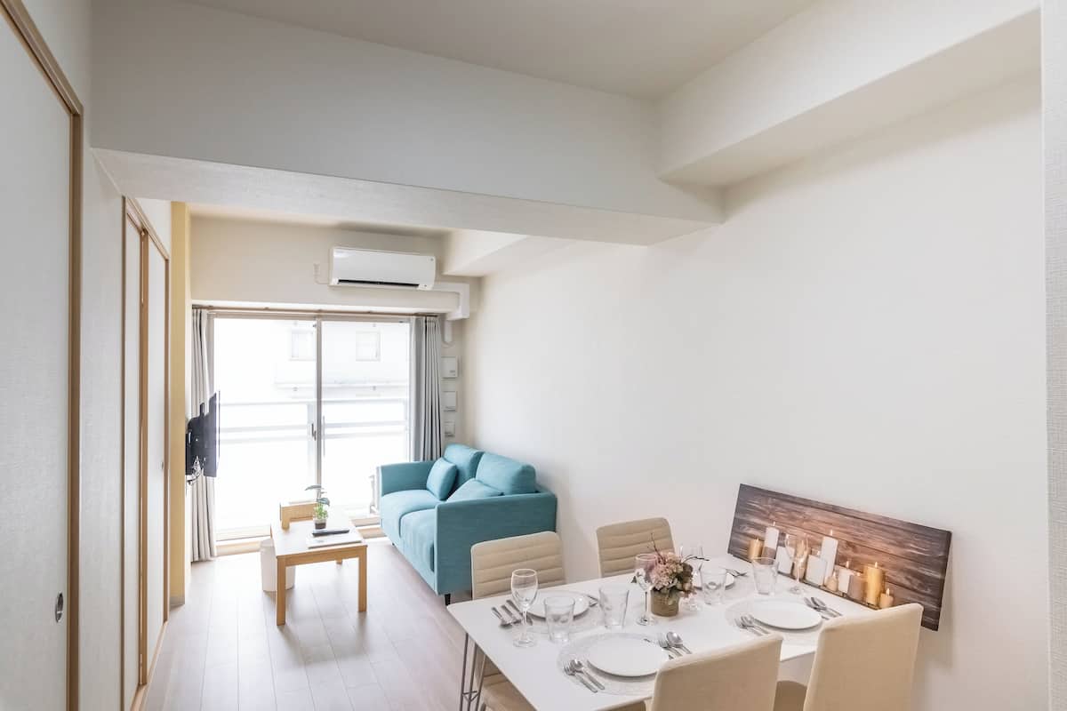 Un espace de repas moderne avec une table dressée pour quatre personnes, un canapé bleu et un tableau représentant un paysage urbain accroché au mur.