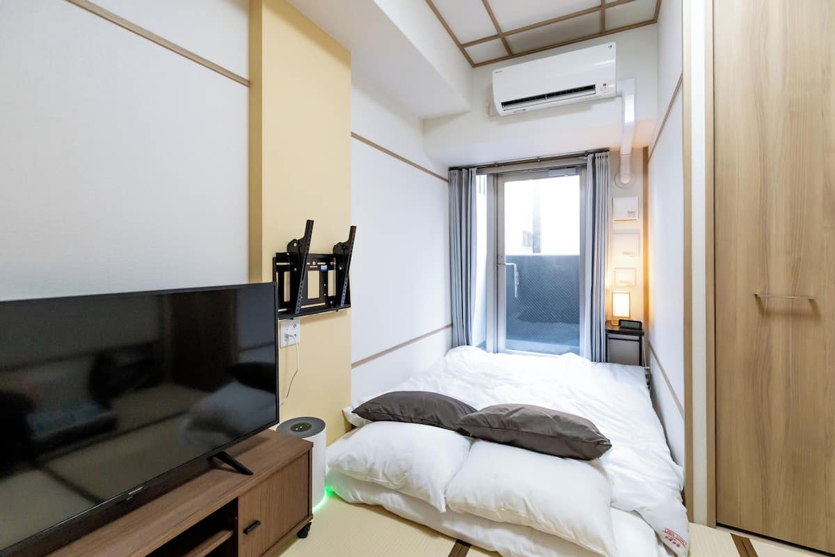 Une chambre d’hôtel de taille réduite, équipée d’un lit, d’une télévision, d’une table de chevet et d’un appareil de climatisation.