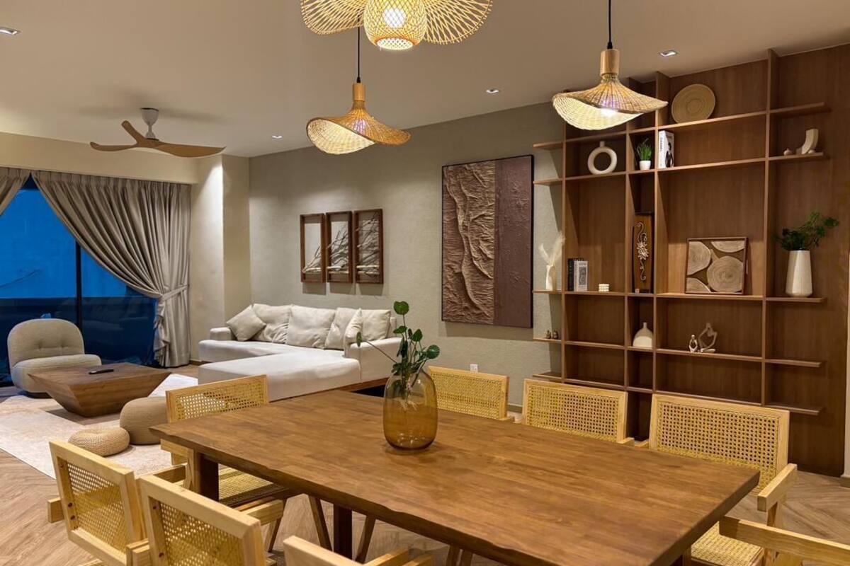 Een moderne woonkamer met een houten eettafel, rieten stoelen, een bank en een boekenkast.