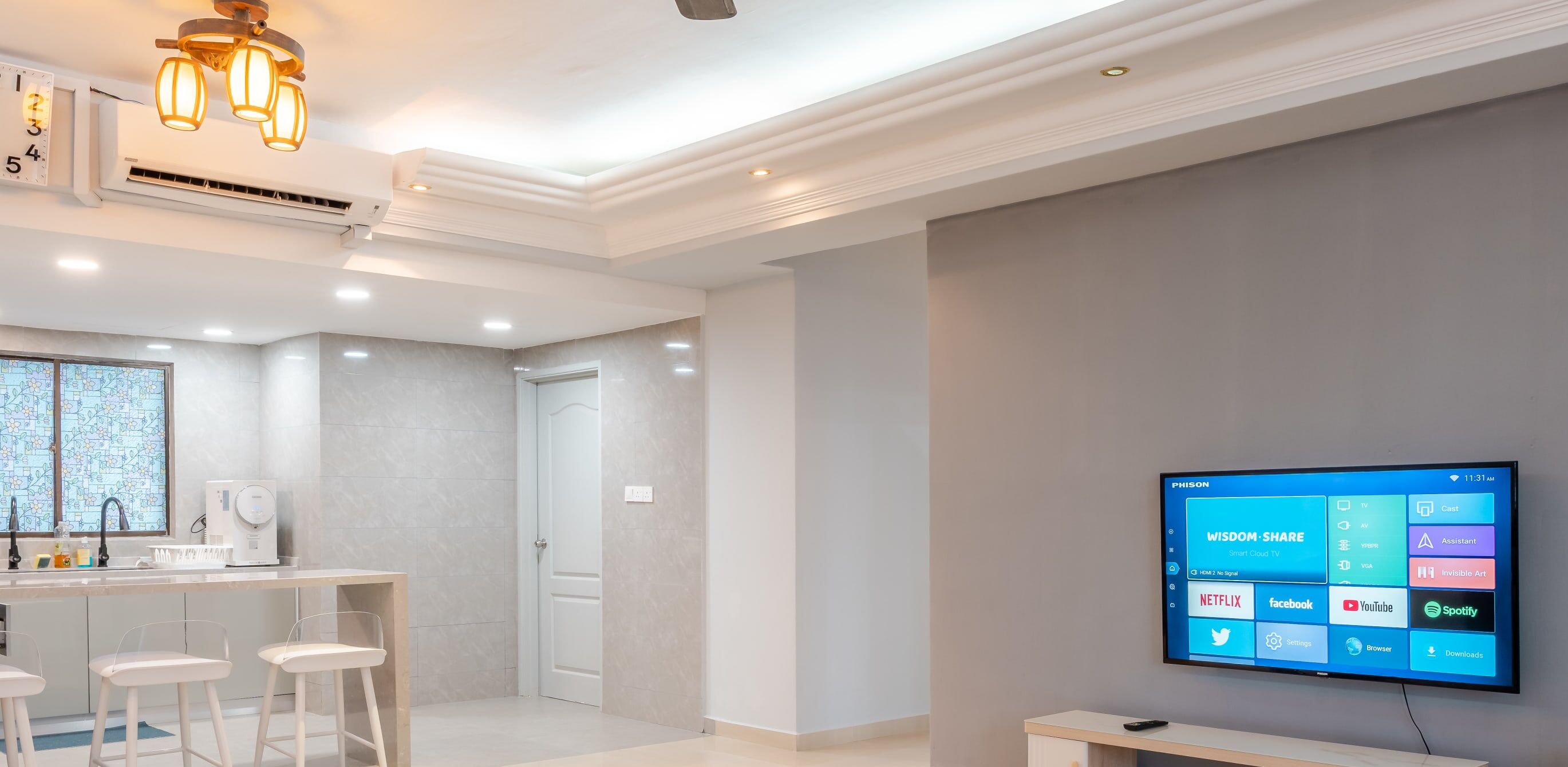 Une chambre d’hôtel moderne dotée d’un grand téléviseur à écran plat diffusant divers services de streaming, d’un coin cuisine avec une carte accrochée au mur et d’un espace salon avec des chaises blanches.