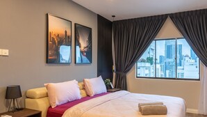 Une chambre d’hôtel avec un grand lit, deux oreillers, un plaid rouge, une table de chevet avec une lampe et une fenêtre avec des rideaux.