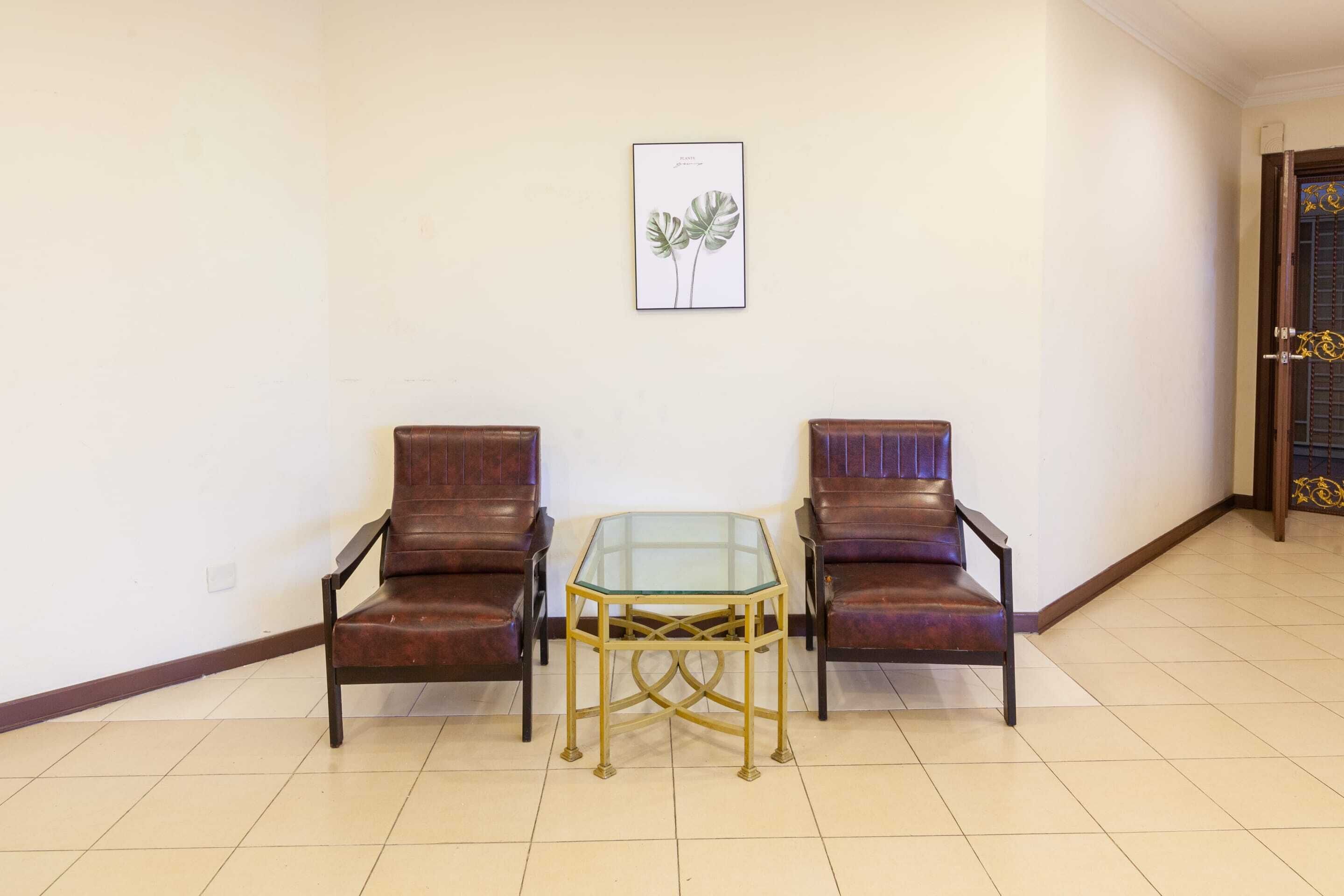 Une pièce comprenant deux fauteuils en cuir, une table à plateau en verre et une estampe botanique encadrée accrochée au mur.