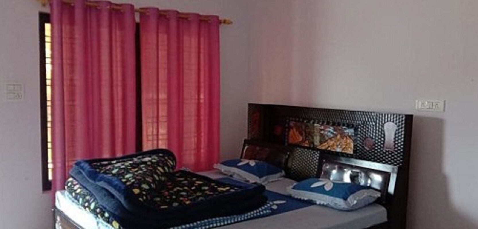 A bedroom with a bed, pink curtains, and a headboard with a patterned design.
