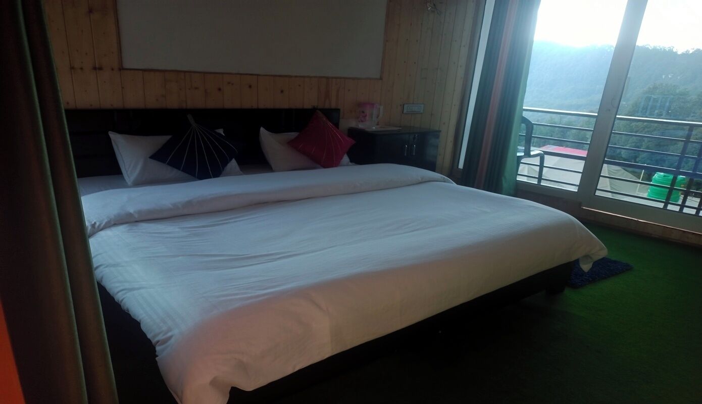 Ein Hotelzimmer mit einem großen Bett, Holzwandverkleidung, einem Nachttisch und Blick auf einen Balkon mit Sitzgelegenheit.