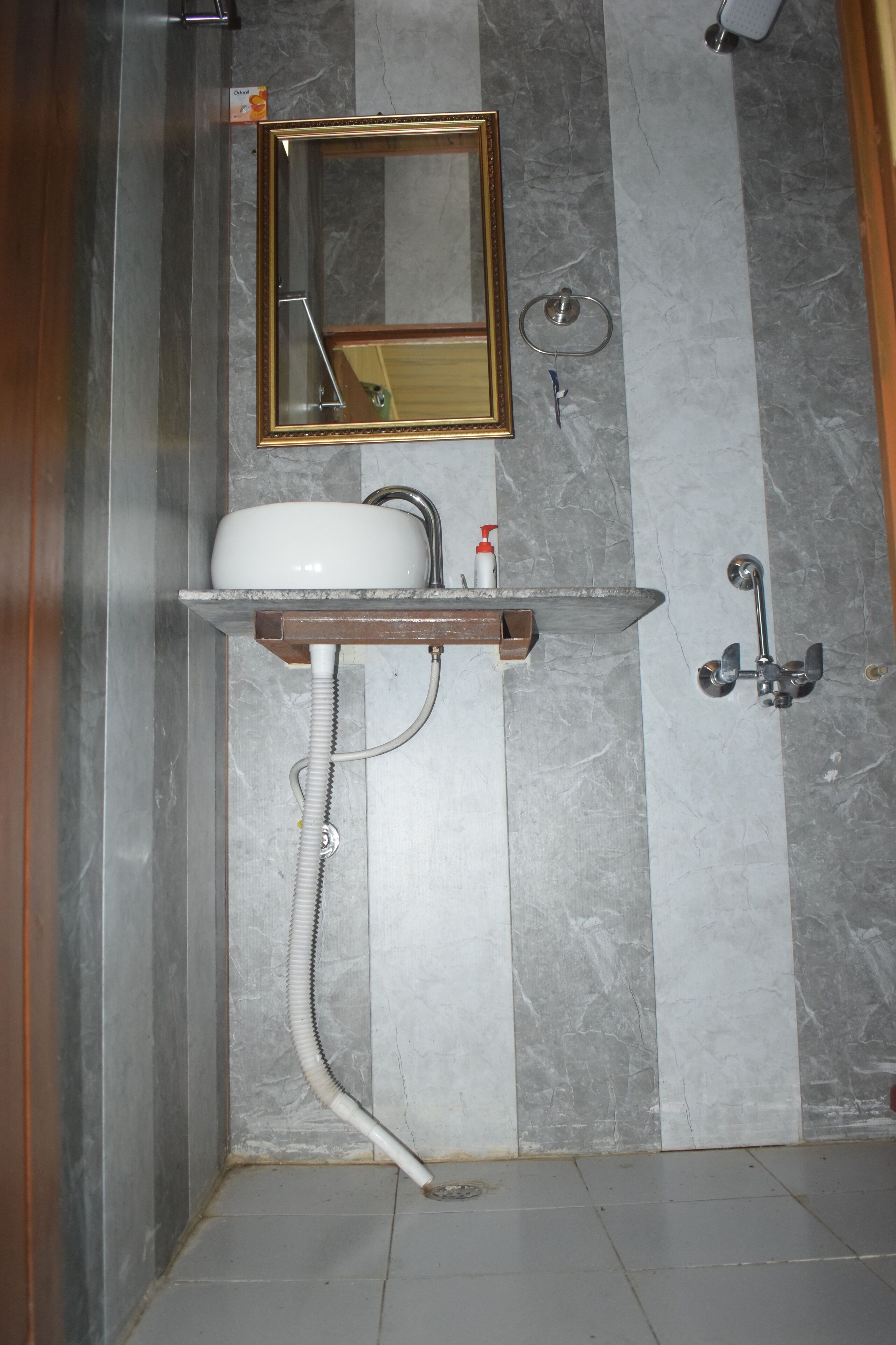 A bathroom with a marble wall, a sink with a mirror, a handheld showerhead, and a towel rack.