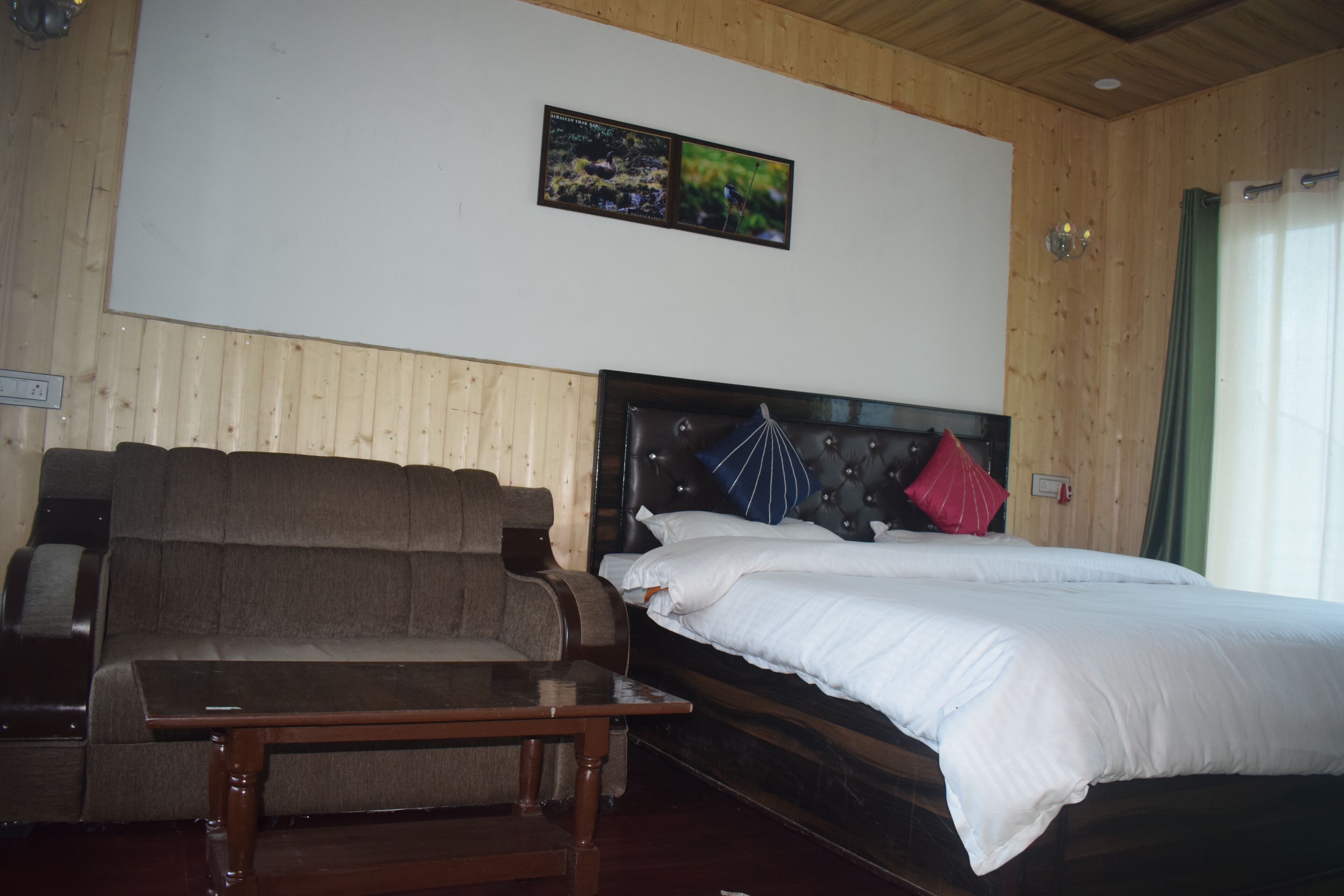A bedroom with a bed, a sofa, and a small table. There is a wall-mounted picture above the bed.