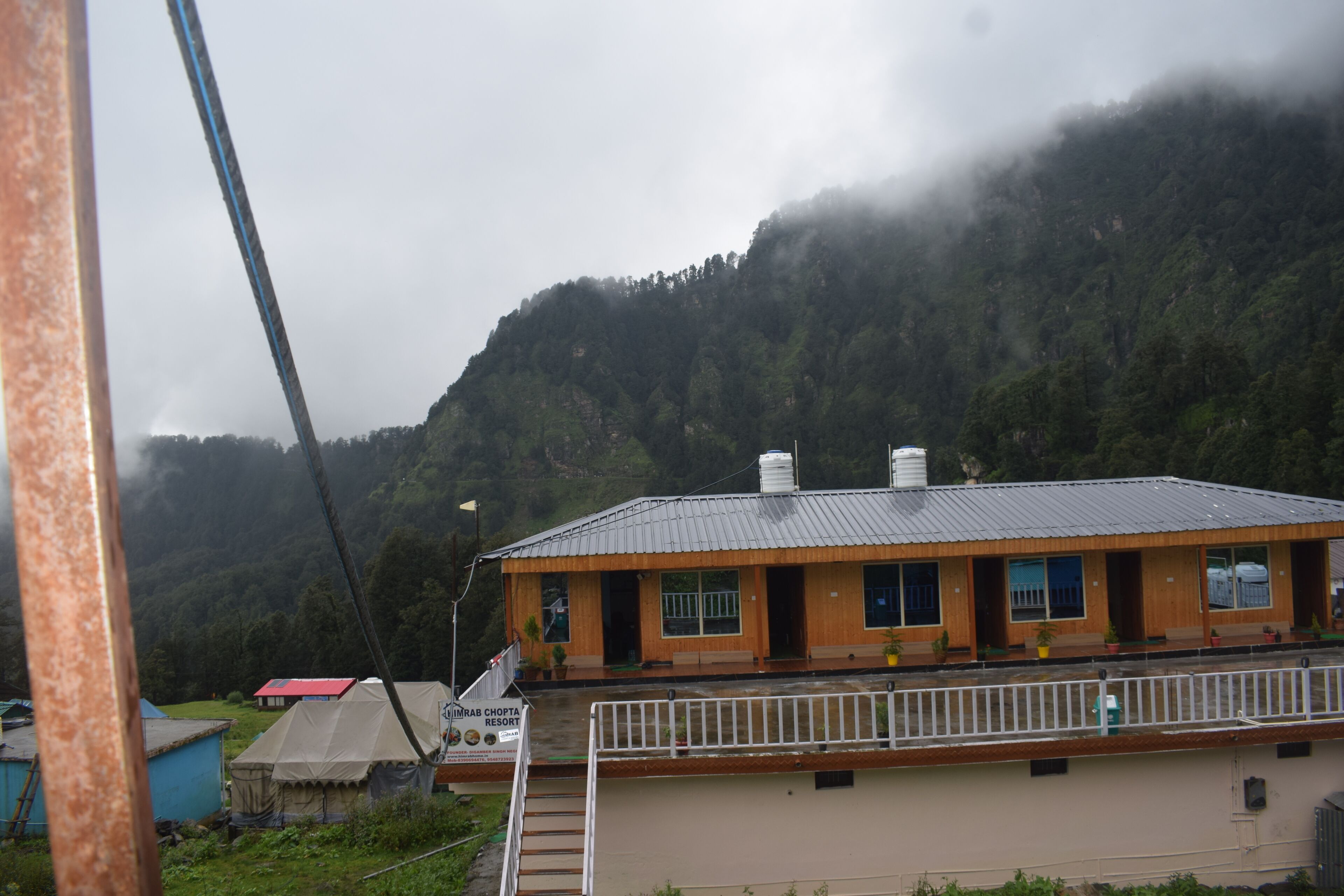 Un bâtiment à deux étages doté d’un balcon, d’une enseigne indiquant qu’il s’agit d’un complexe hôtelier, et avec une chaîne de montagnes en arrière-plan.